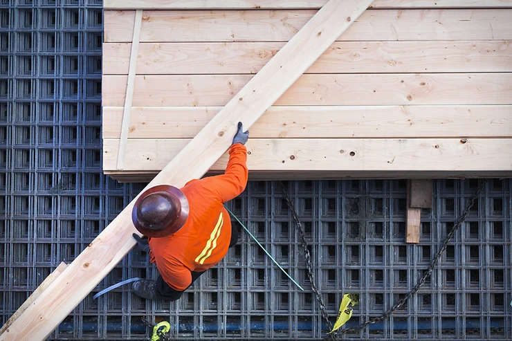 A man in high-vis jacket and helmet cutting wood on a pallet of other planks of wood